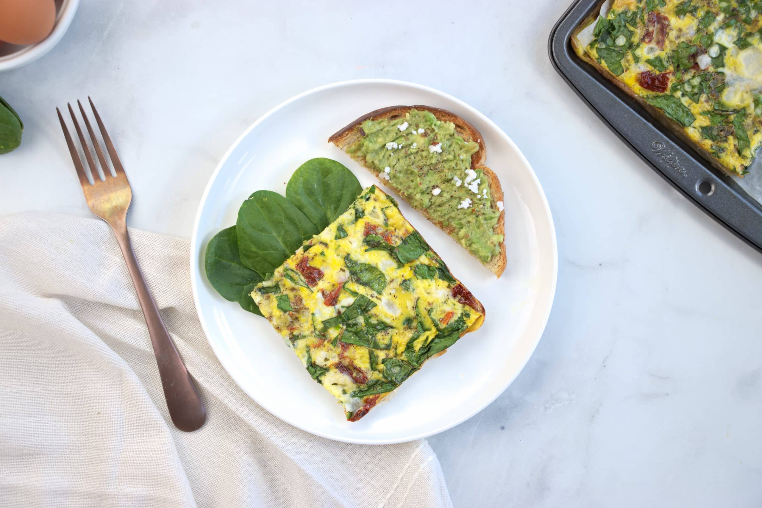 a piece of spinach and feta frittata on a plate served with avocado toast