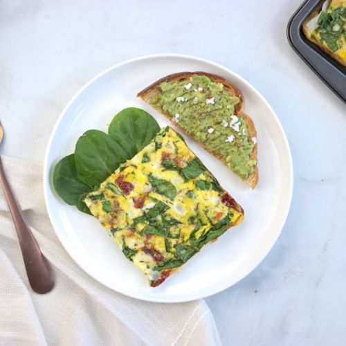a piece of spinach and feta frittata on a white plate served with half an avocado toast.